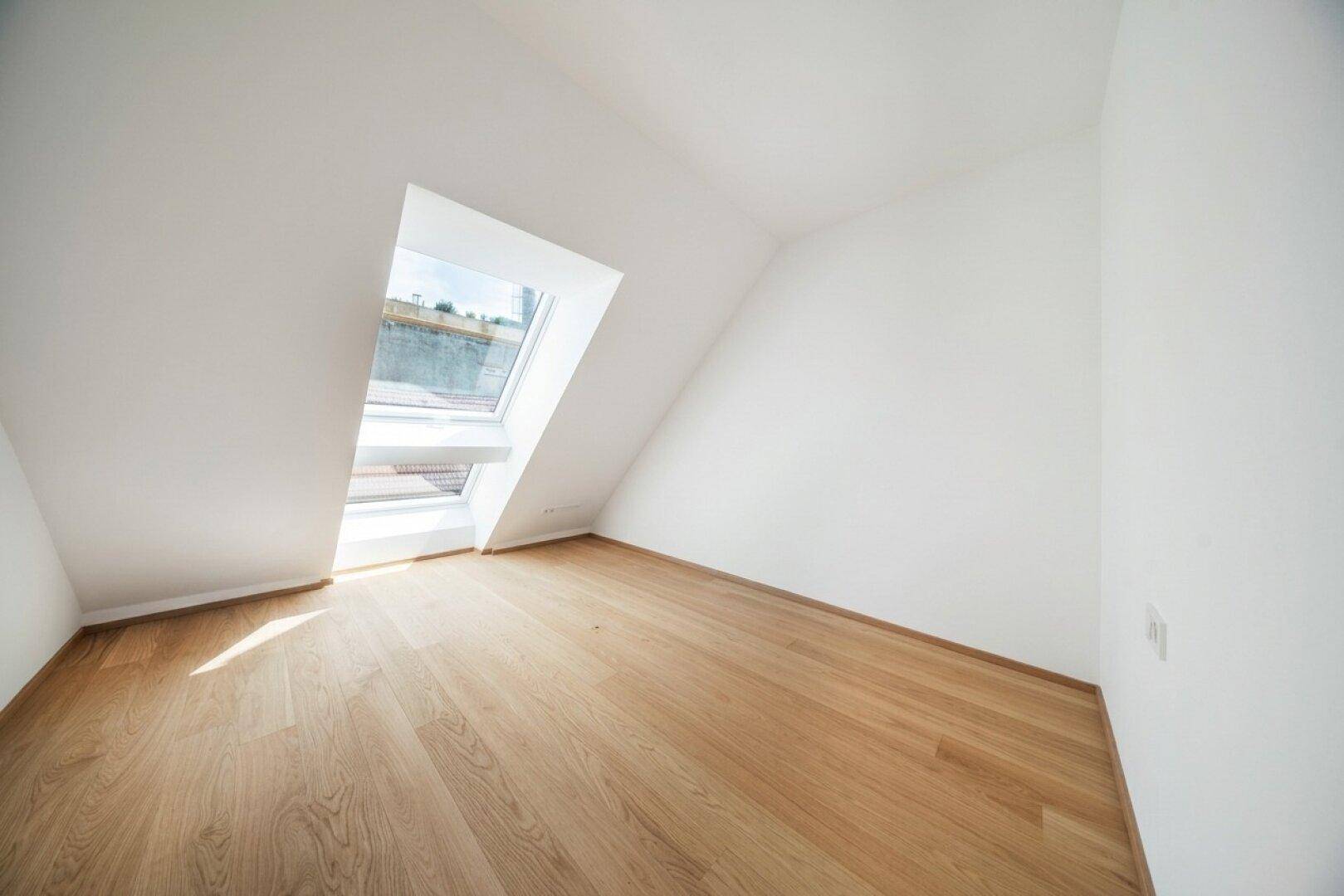 Helles Dachzimmer mit schrägen Wänden, Holzboden und großem Dachfenster für viel Licht.