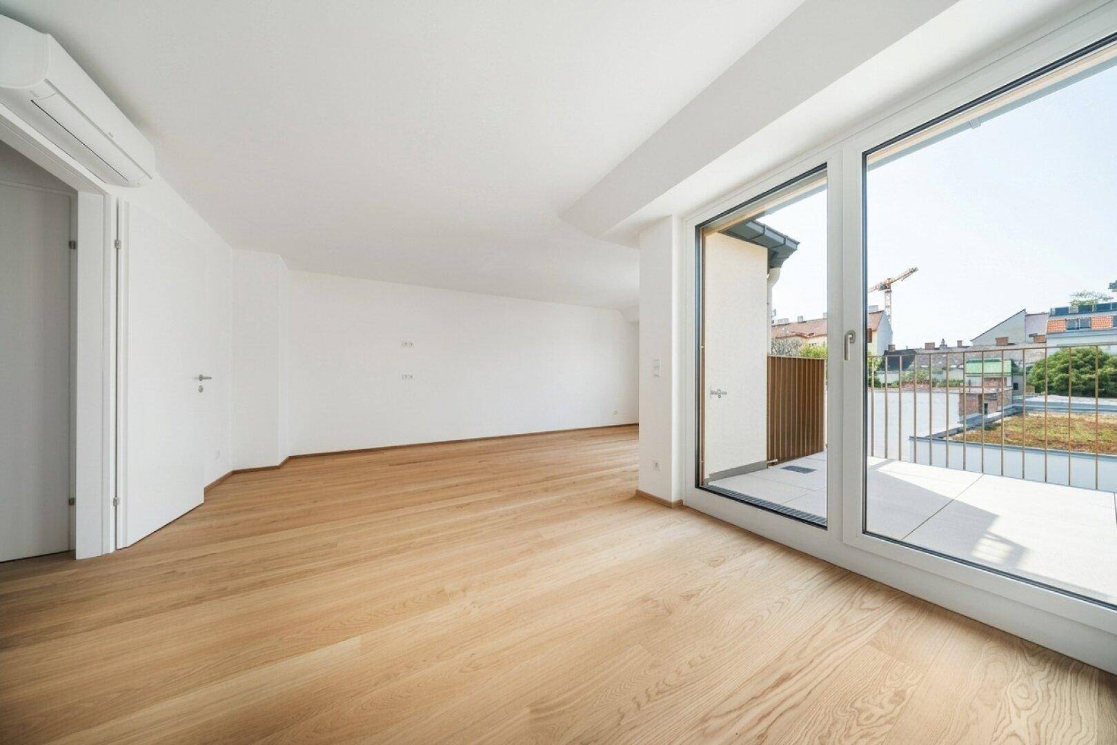 Helles Zimmer mit Holzboden und Zugang zu einem Balkon, bietet viel natürliches Licht.
