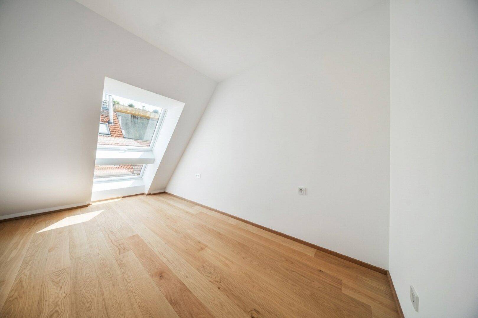 Helles Dachzimmer mit Holzboden und großem Dachfenster, das den Raum mit natürlichem Licht durchflutet.