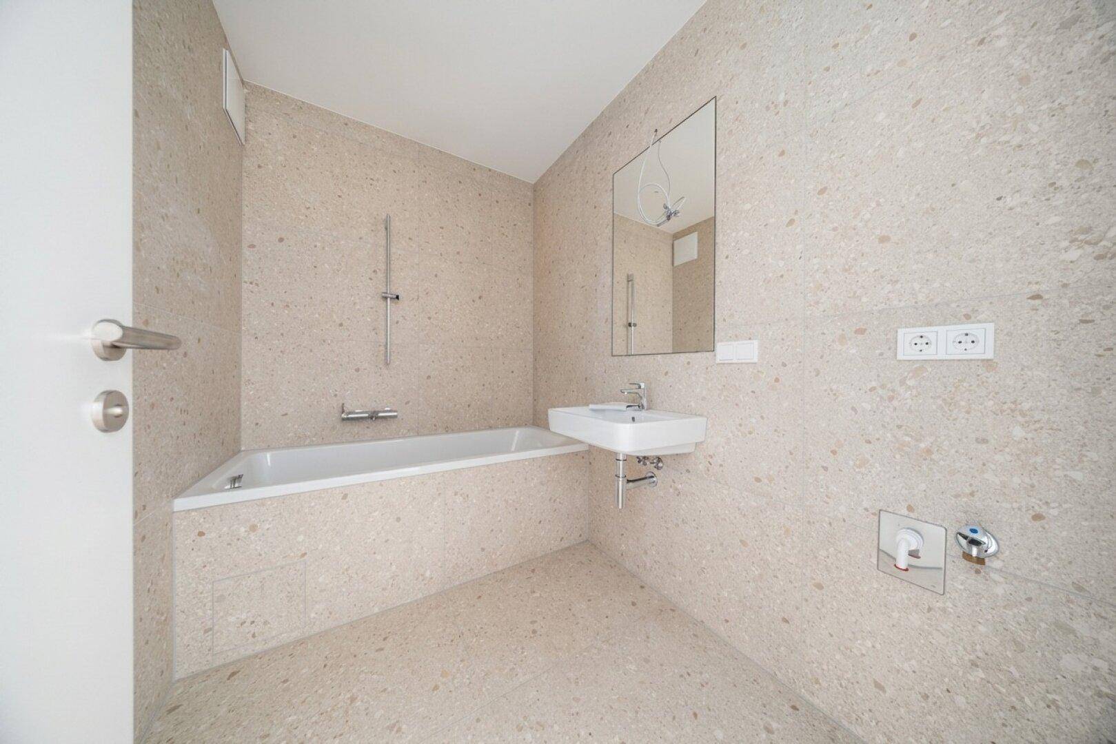 Modernes Badezimmer mit beigefarbenen Fliesen, Badewanne und Waschbecken, in neuwertigem Zustand.