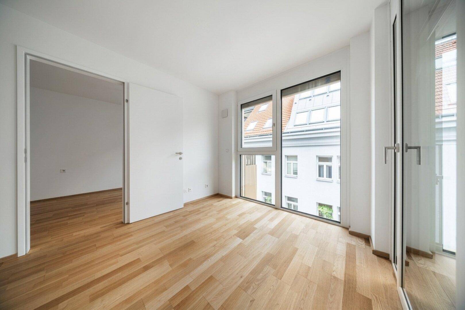 Geräumiges, helles Zimmer mit Holzboden und großen Fenstern, ideal als Schlafzimmer.