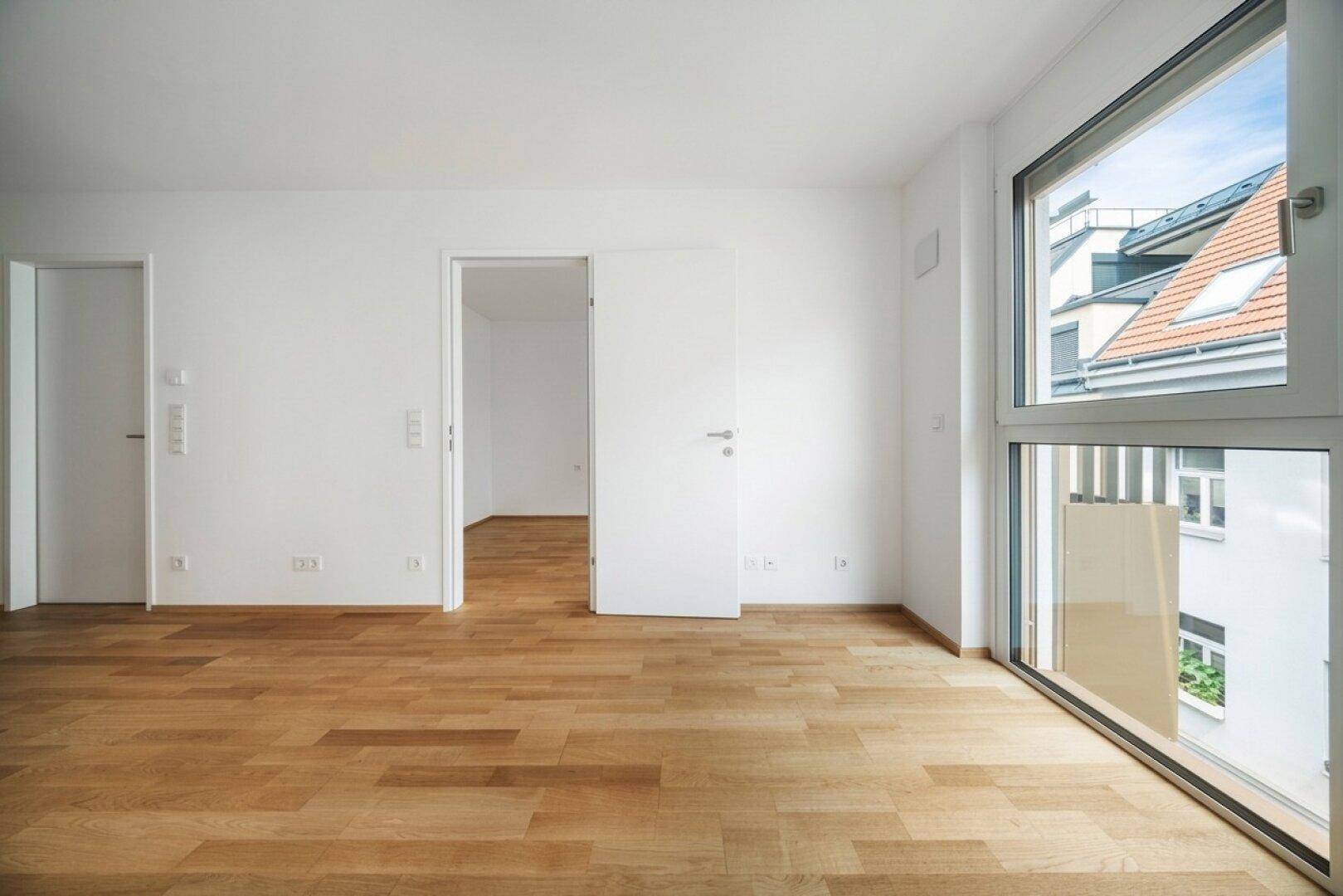 Lichtdurchfluteter Wohnbereich mit Holzboden und bodentiefen Fenstern, bietet viel Tageslicht.