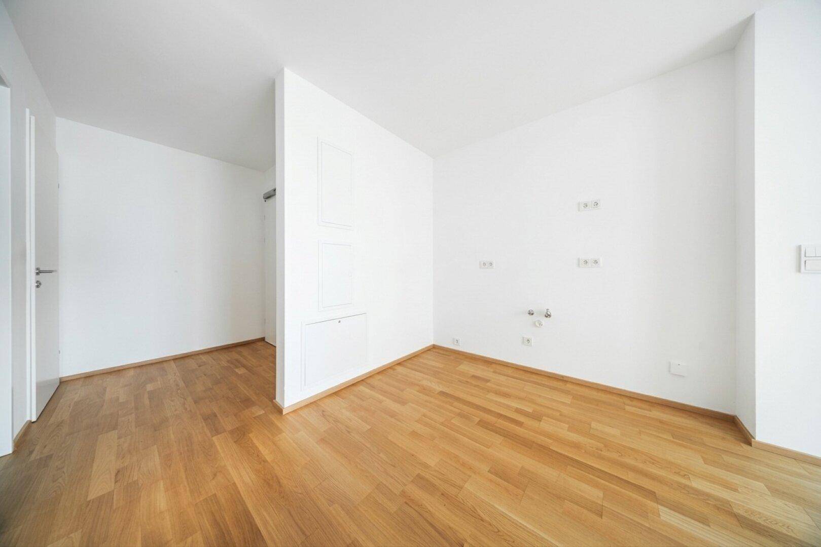 Leerer Raum mit Parkettboden und weißen Wänden, mit integrierten Wandpaneelen und Anschlüssen.