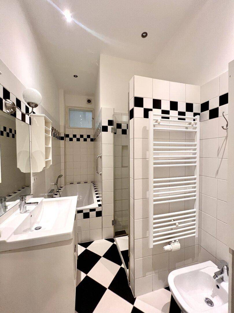 Modernes Badezimmer mit schwarz-weißem Fliesenmuster, Badewanne, Dusche und beheiztem Handtuchhalter.