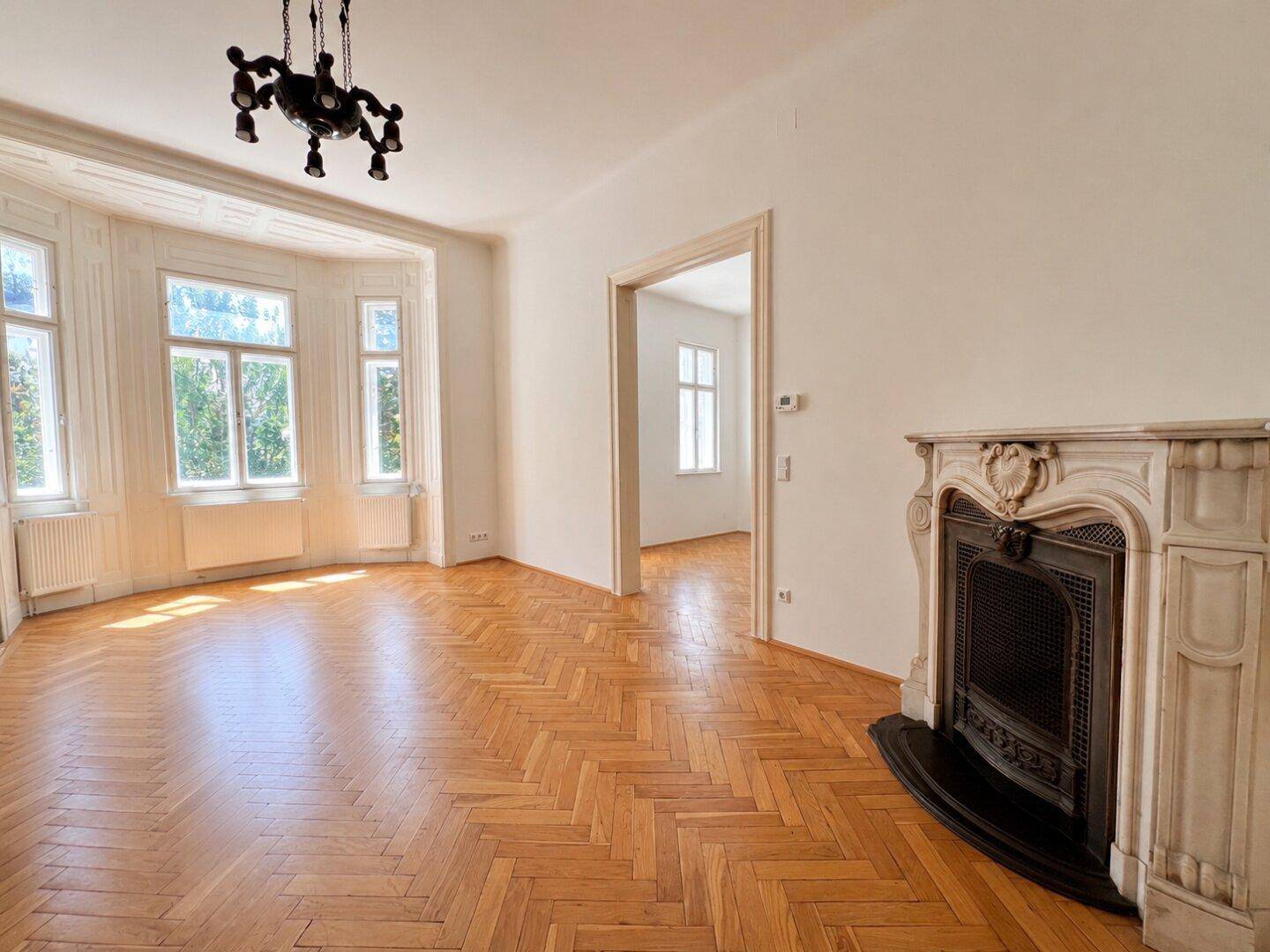 Elegantes Wohnzimmer mit Fischgrätparkett, Erkerfenstern und einem dekorativen Kamin, der Charme verleiht.