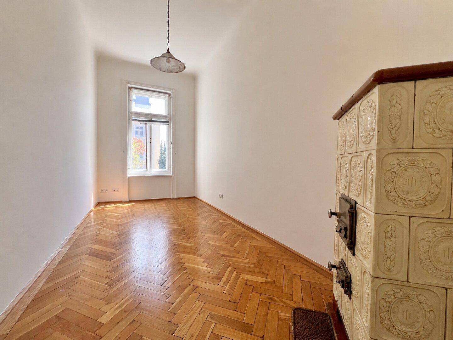 Helles Zimmer mit Fischgrätparkett und traditionellem Kachelofen, ideal als Schlaf- oder Arbeitszimmer.