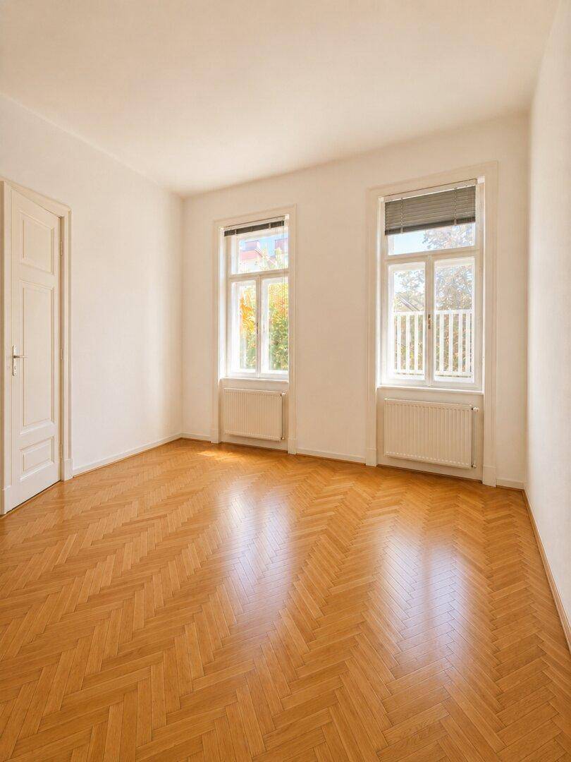 Helles Zimmer mit Fischgrätparkett und zwei großen Fenstern, die viel Tageslicht bieten.