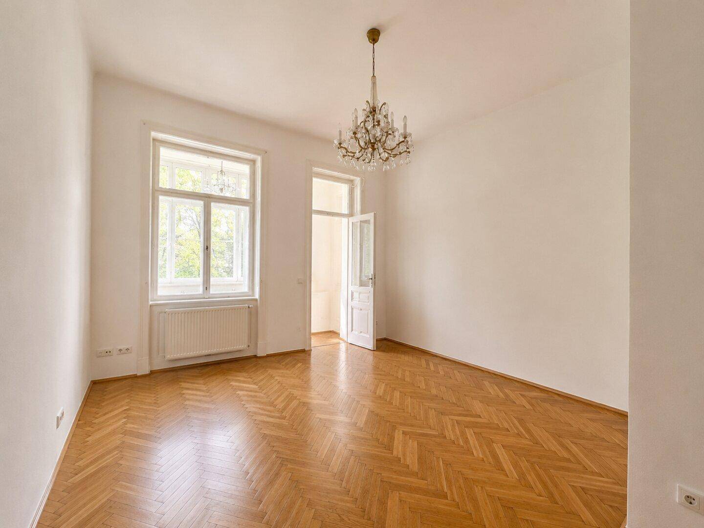 Geräumiges Zimmer mit Fischgrätparkett, Kronleuchter und großem Fenster, das eine angenehme Atmosphäre schafft.