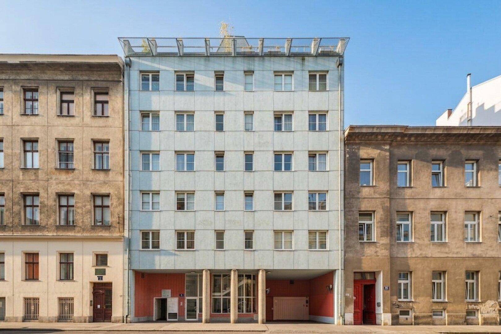 Mehrstöckiges Wohngebäude mit heller Fassade und vielen Fenstern in urbaner Umgebung.