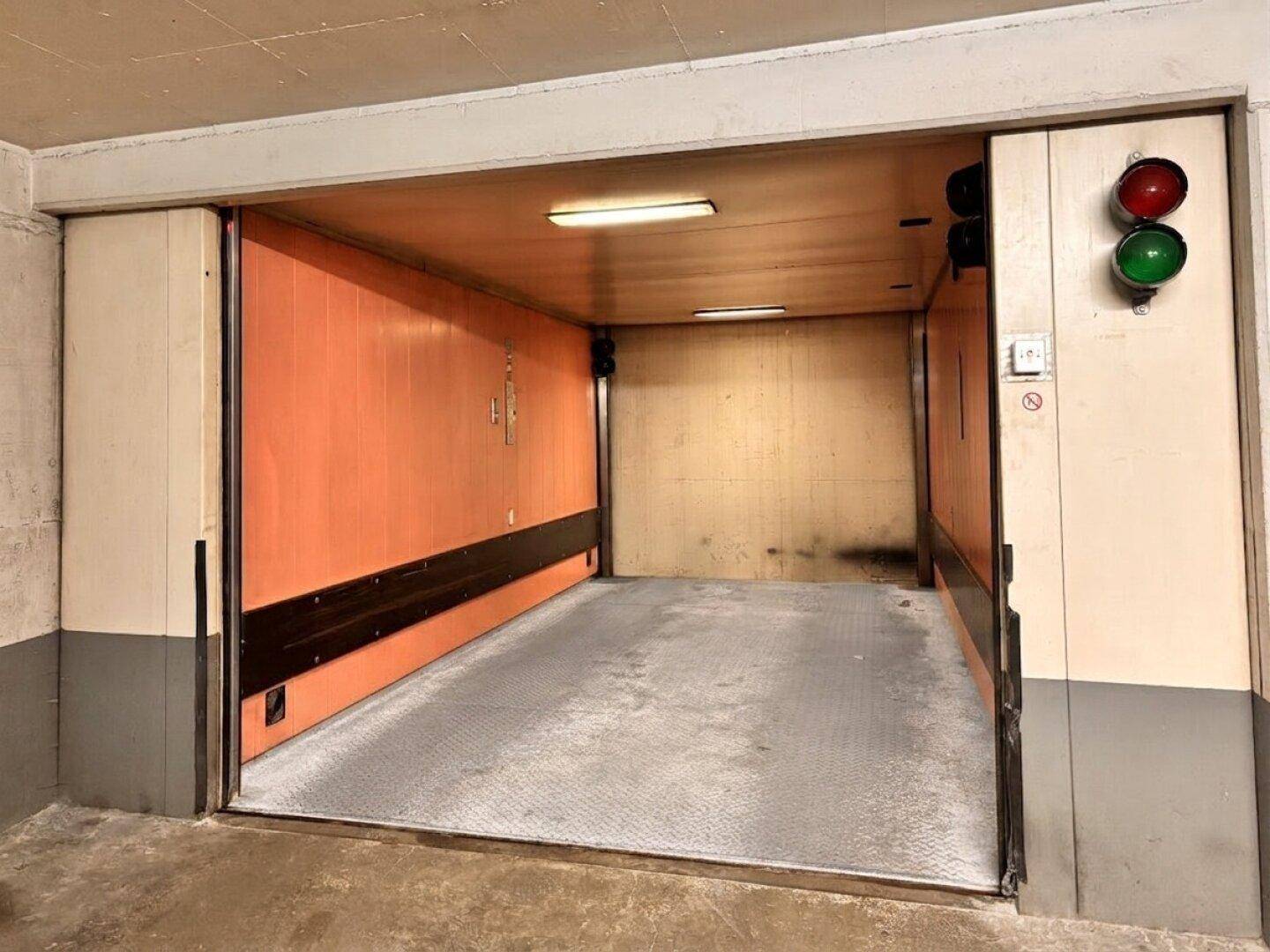 Autoaufzug in einer Tiefgarage mit orangefarbenen Wänden und Kontrollleuchten.