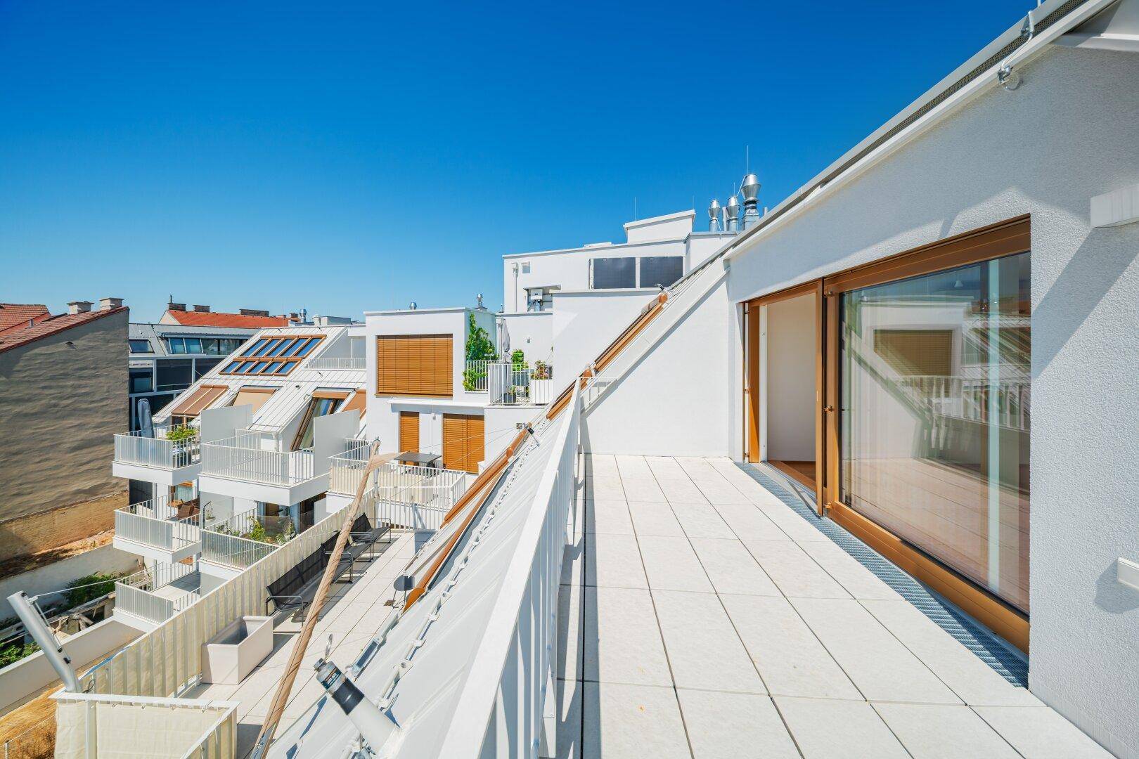 Lange Dachterrasse mit Fliesenboden und Blick auf die umliegenden modernen Gebäude.
