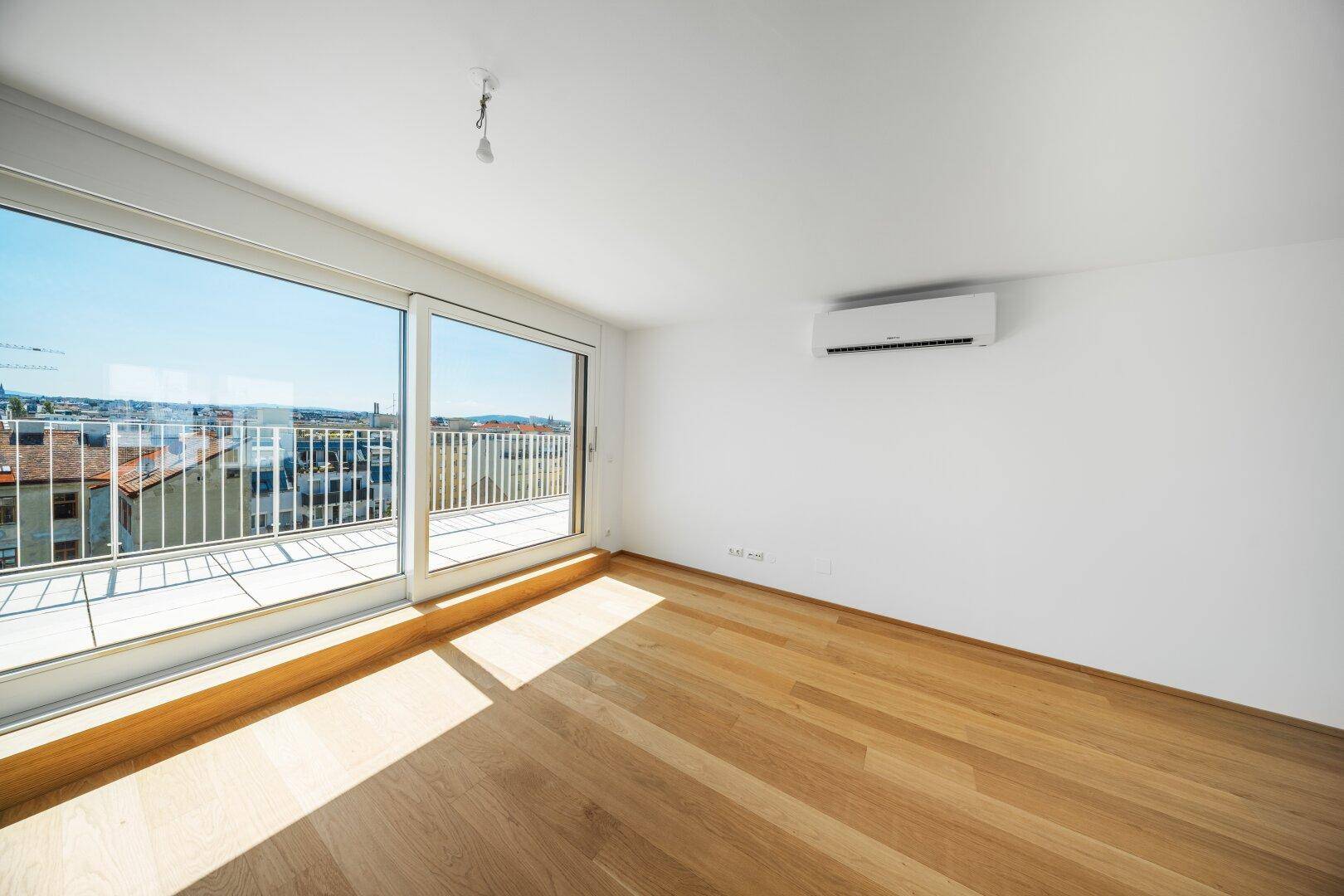 Lichtdurchfluteter Raum mit Holzboden, Klimaanlage und Schiebetür zur Terrasse.