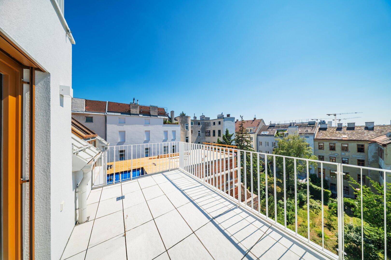 Heller Balkon mit weißem Geländer und Blick auf die umliegenden Gebäude und Grünflächen.
