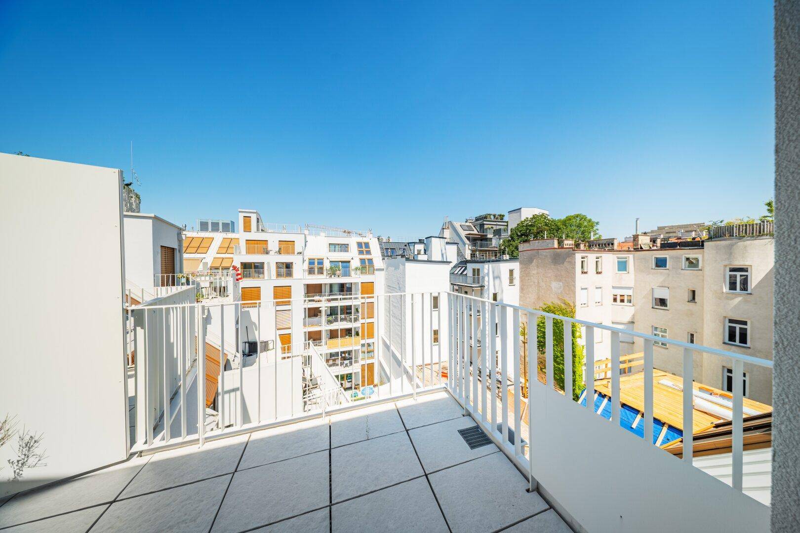 Sonniger Balkon mit Fliesenboden und weitem Blick über die Dächer der Stadt.