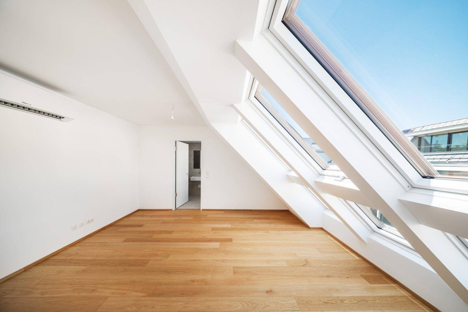 Heller Raum im Dachgeschoss mit großen Dachfenstern, Holzboden und Klimaanlage.