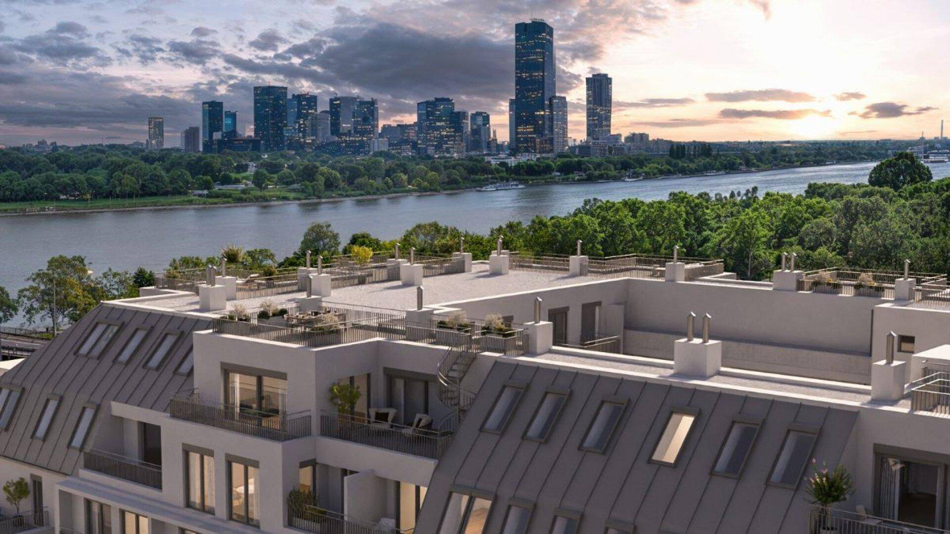 Moderne Wohnanlage mit Mansarddach, Balkonen und Dachterrassen, mit Blick auf die Stadt und den Fluss.
