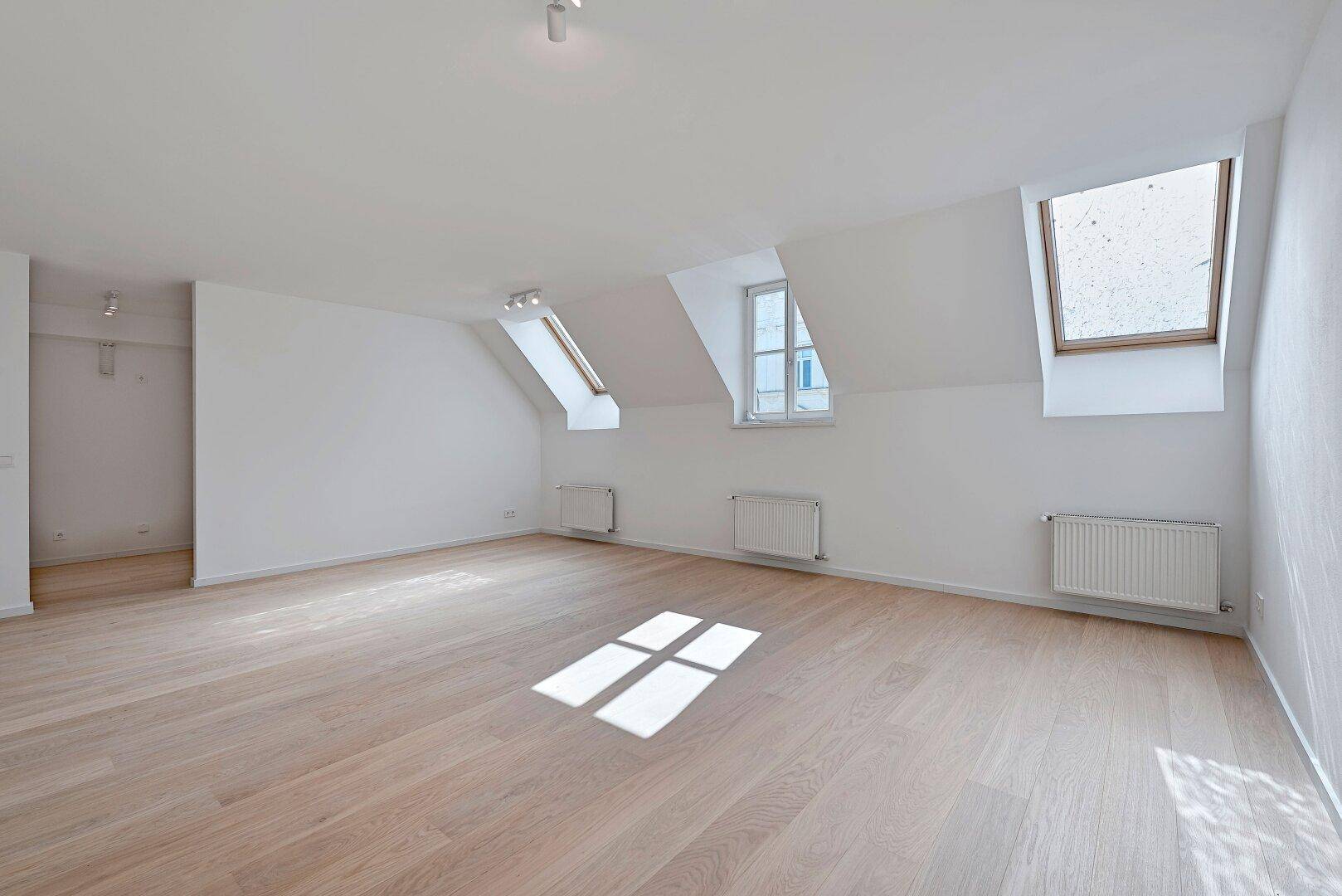 Geräumiges Zimmer mit Dachschrägen, hellen Holzböden und viel Tageslicht durch die Dachfenster.