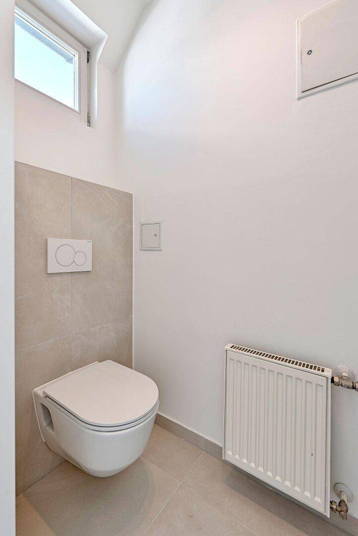 Modernes Gäste-WC mit wandhängender Toilette, grauen Fliesen und kleinem Fenster.