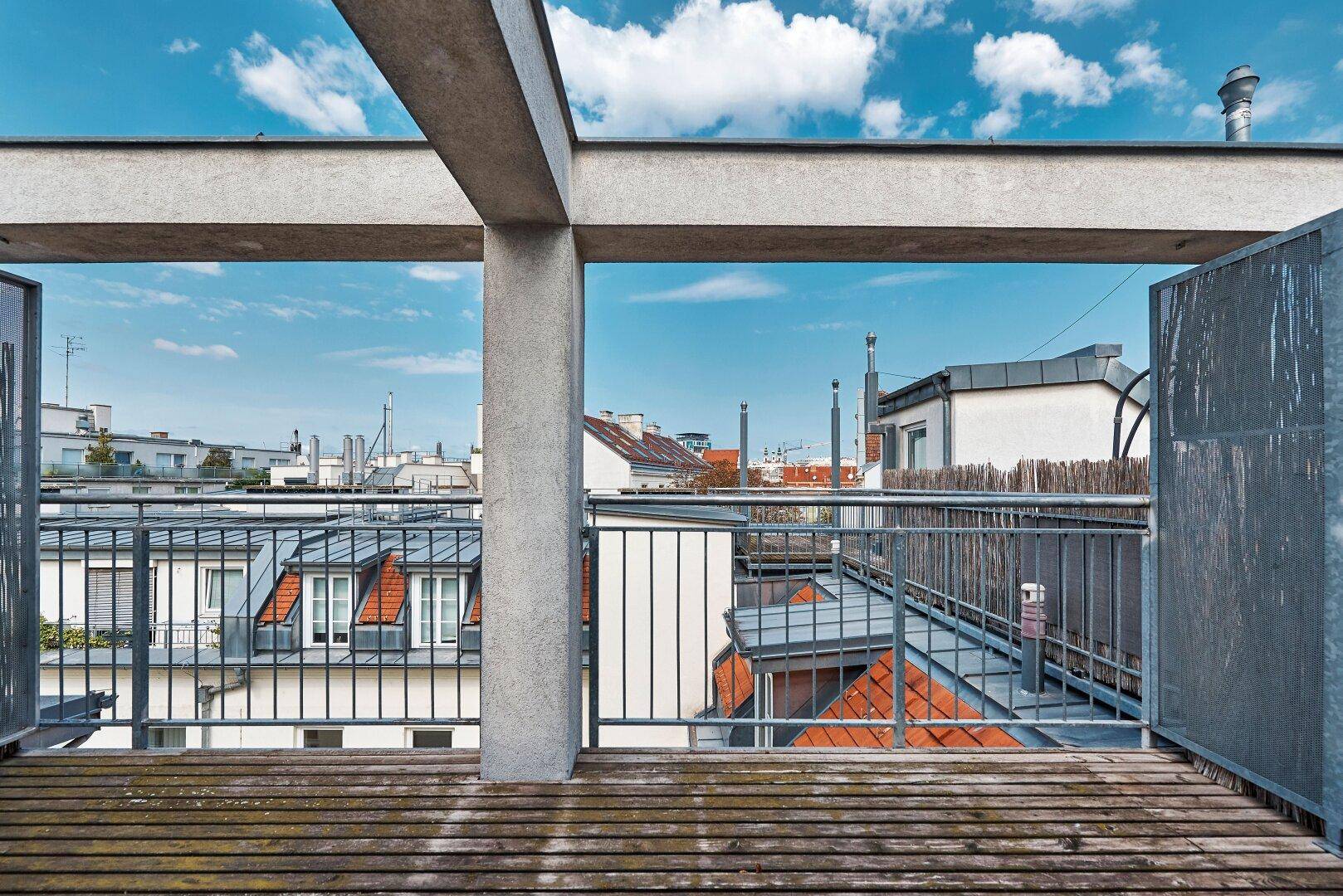 Dachterrasse mit Holzbelag und Blick über die städtische Umgebung unter blauem Himmel.