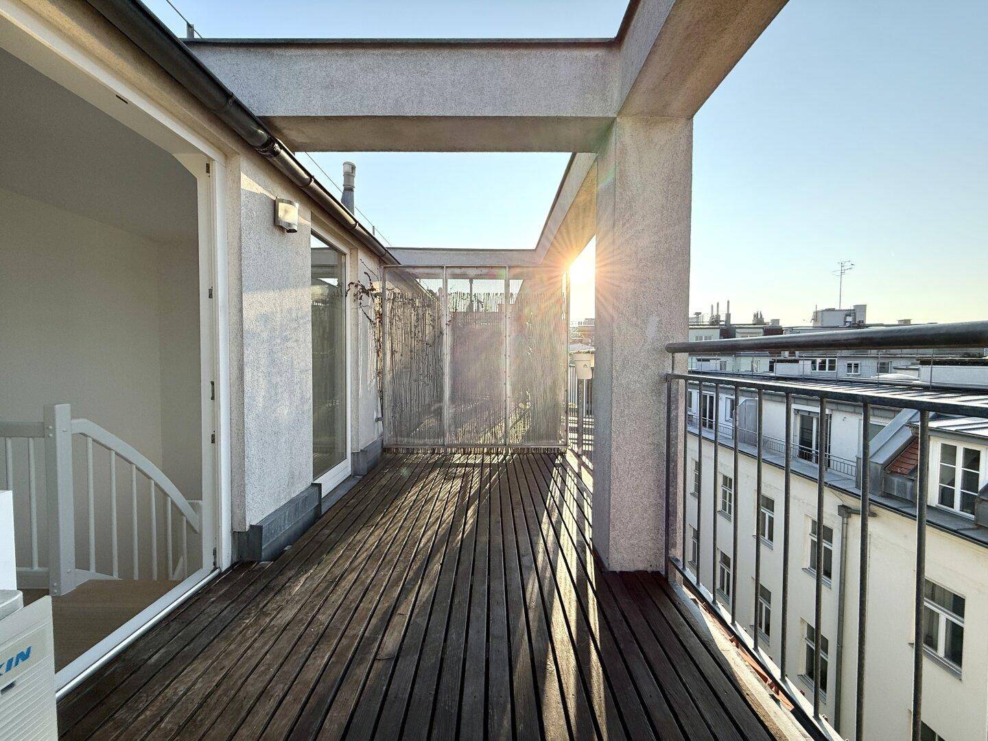 Sonniger Balkon mit Holzbelag und weitem Blick über die Dächer der Stadt.