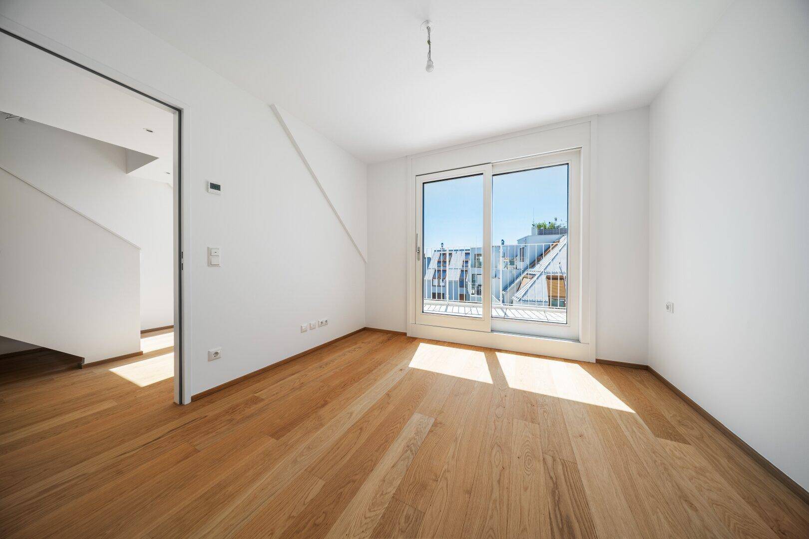 Helles Schlafzimmer mit Holzboden und Zugang zu einem französischen Balkon.