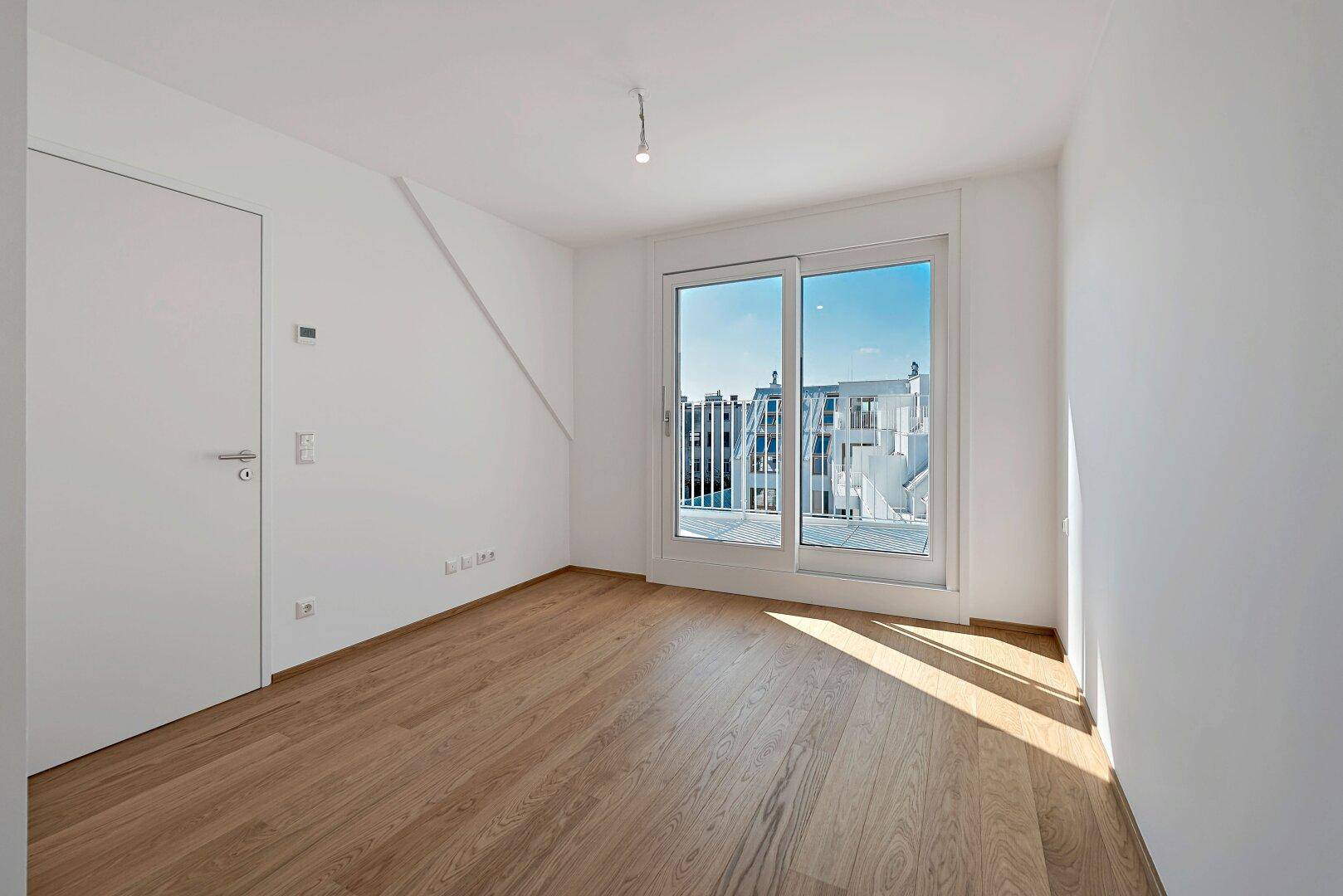 Heller Raum mit Holzboden und Zugang zu einem Balkon, ideal als Schlafzimmer.
