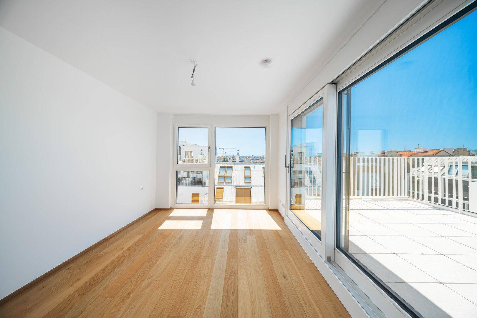 Lichtdurchflutetes Zimmer mit großen Fenstern, Terrassenzugang und Holzboden.