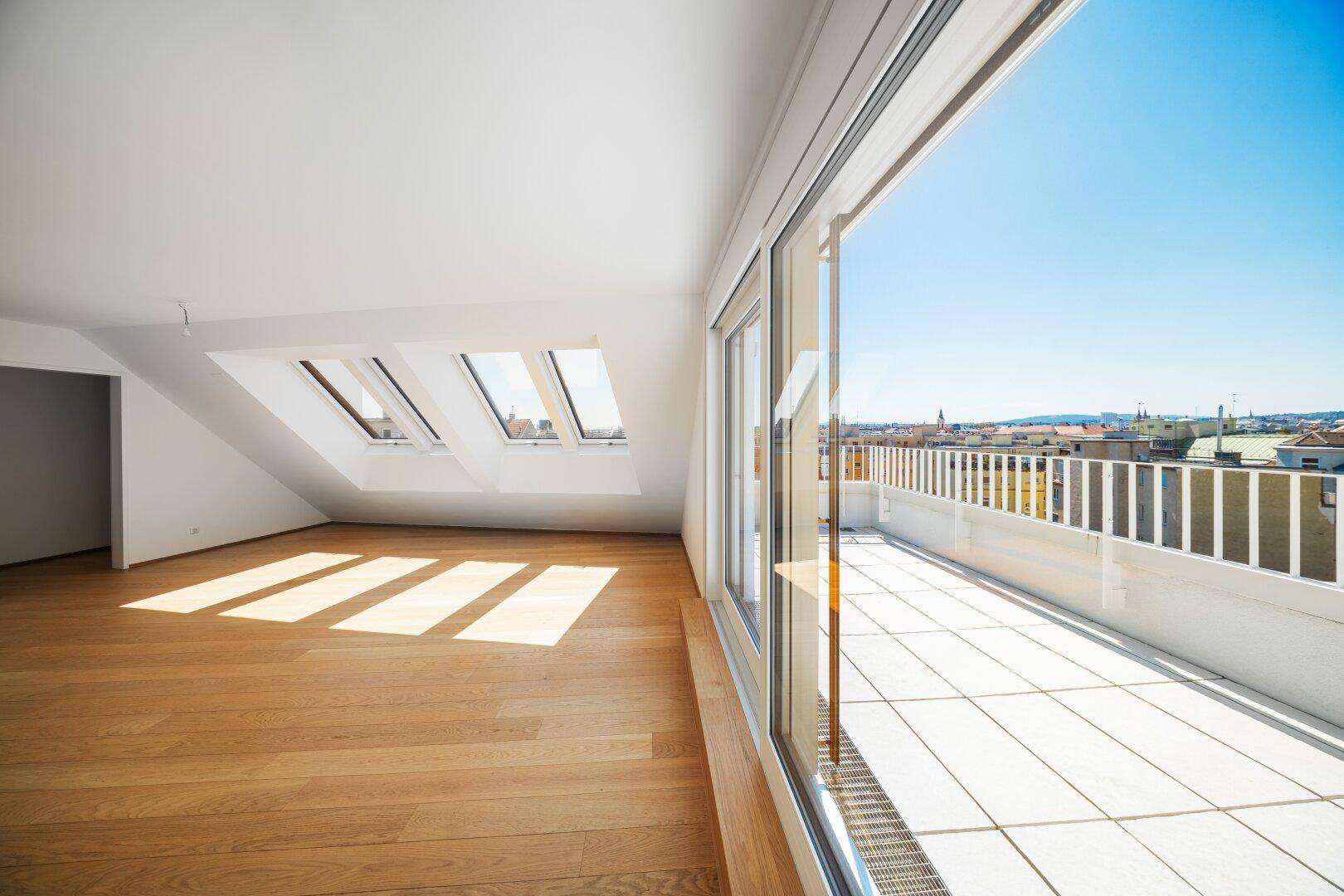 Lichtdurchfluteter Raum im Dachgeschoss mit Holzboden und großer Schiebetür zur sonnigen Terrasse.