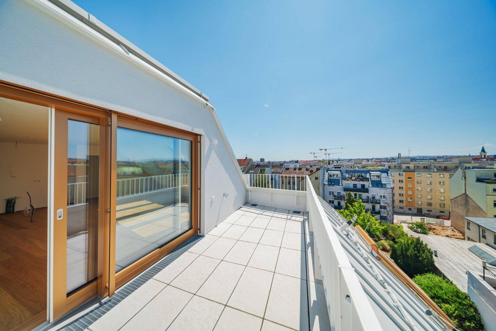 Geräumige Dachterrasse mit hellen Fliesen und weitem Blick über die Stadtlandschaft unter blauem Himmel.
