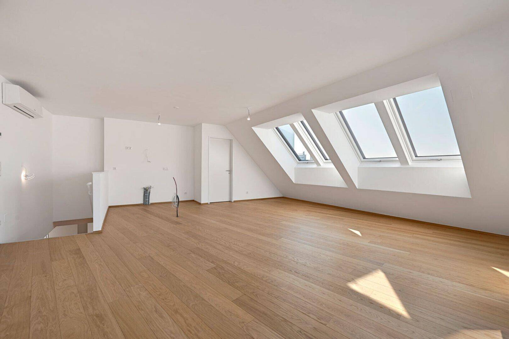 Heller Dachgeschossraum mit Holzboden, Dachfenstern und Klimaanlage, bereit zur individuellen Einrichtung.