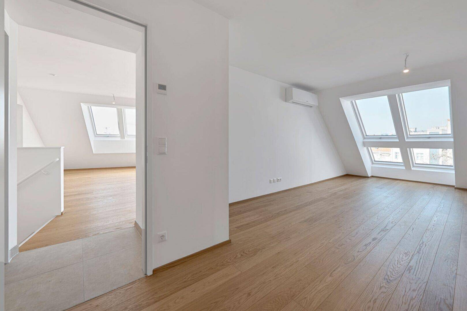 Übergangsbereich mit Holzboden und Blick in einen weiteren hellen Raum mit Dachfenstern und Klimaanlage.