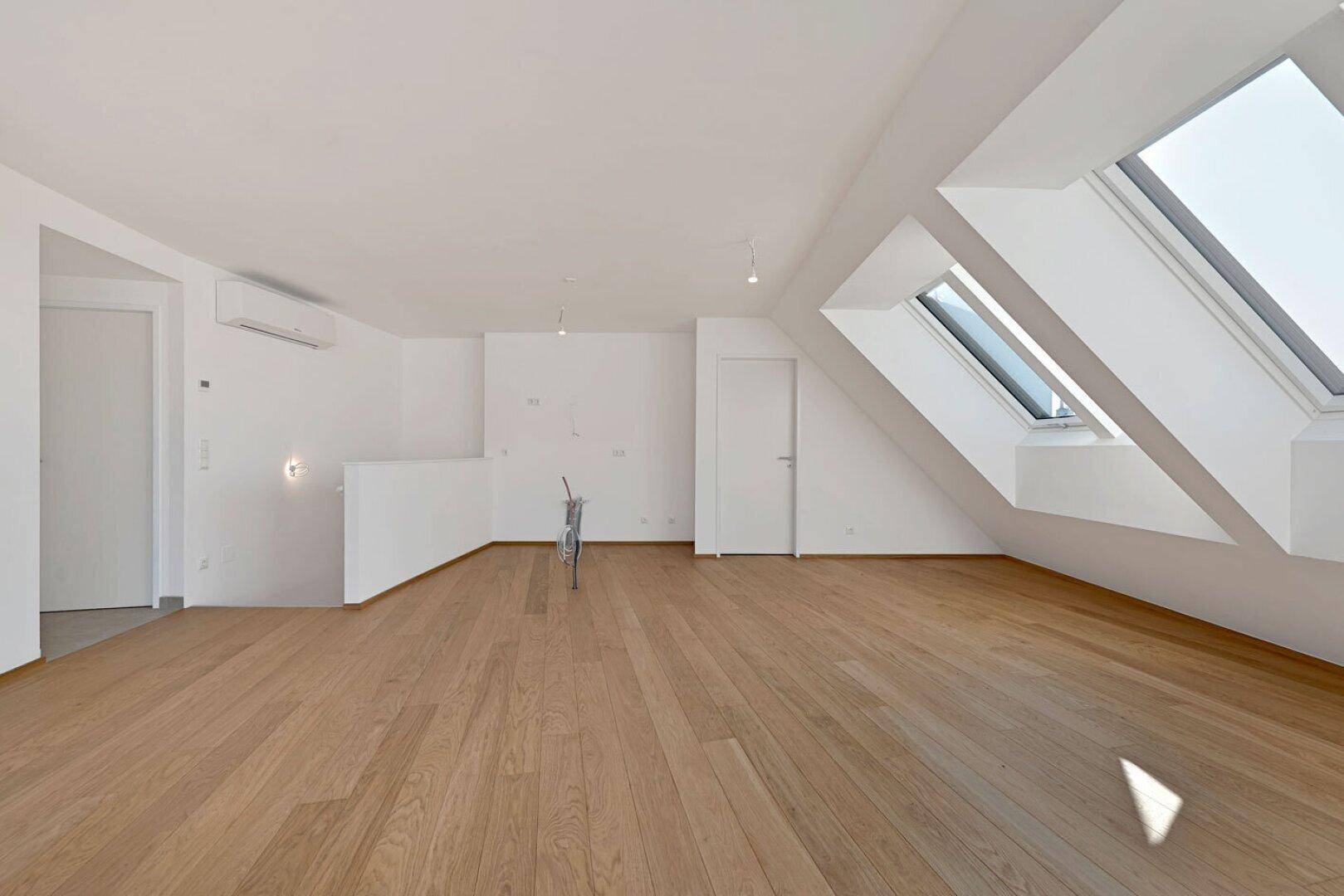 Geräumiges Dachgeschosszimmer mit Holzboden und schrägen Wänden, ideal für offenes Wohnen und viel Licht.