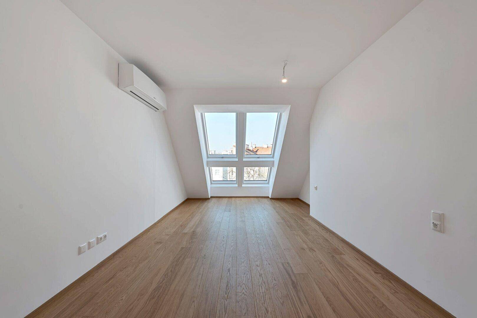Helles Schlafzimmer mit Holzboden, Dachfenster und Klimaanlage, ideal für Ruhe und Komfort.