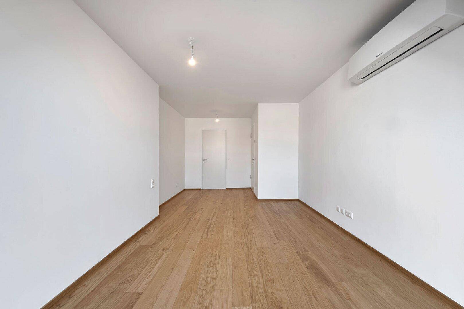 Leeres Zimmer mit Holzboden und Klimaanlage, bereit für individuelle Gestaltung und Nutzung.