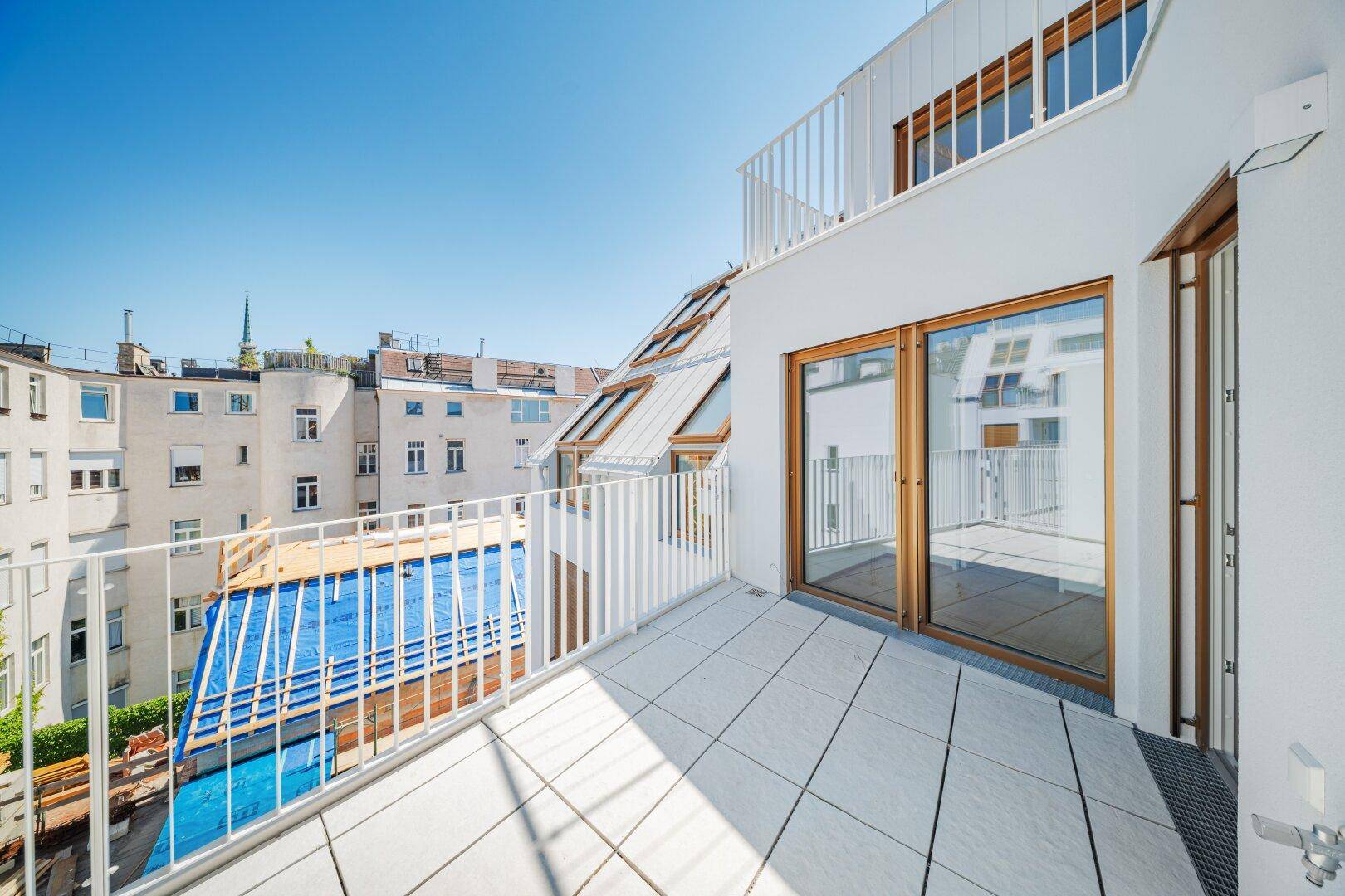 Balkon mit Fliesenboden und Blick auf einen Innenhof mit Pool und umliegende Gebäude.