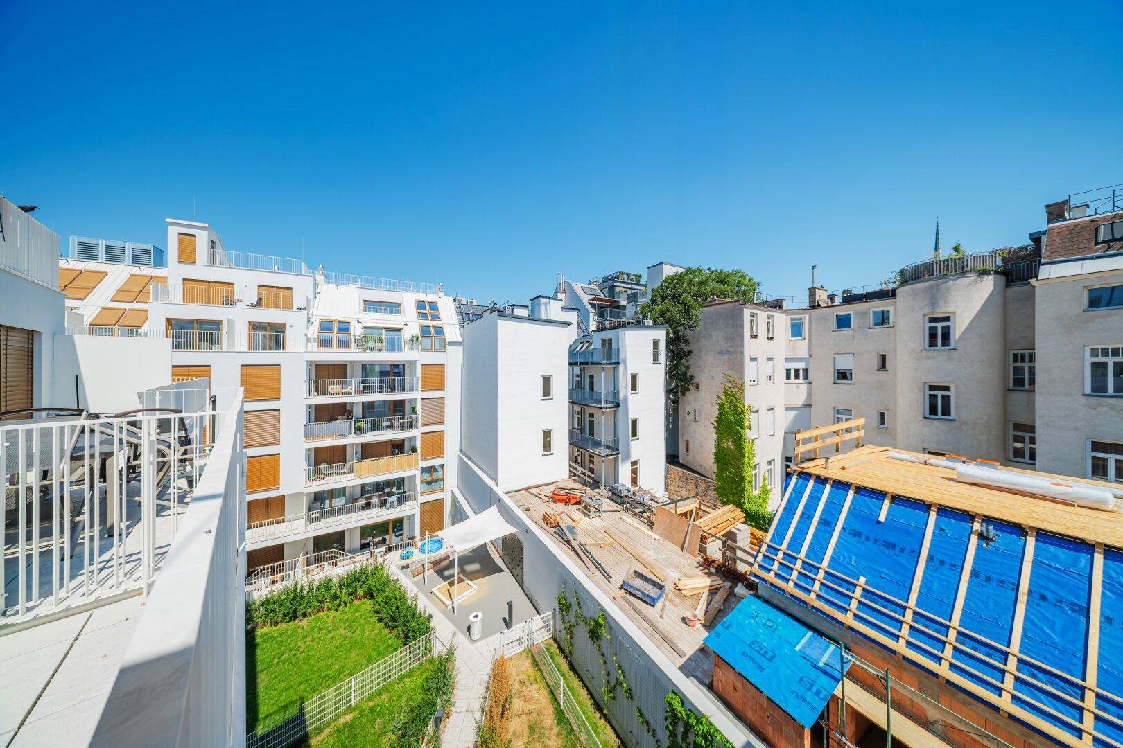 Blick von oben auf einen Innenhof mit Grünflächen, Pool und angrenzenden modernen Gebäuden.
