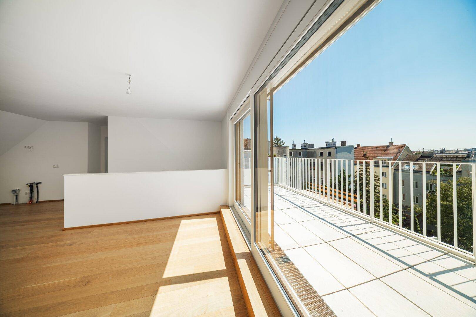 Lichtdurchfluteter Innenraum mit breiter Schiebetür zur sonnigen Dachterrasse und weitem Stadtblick.