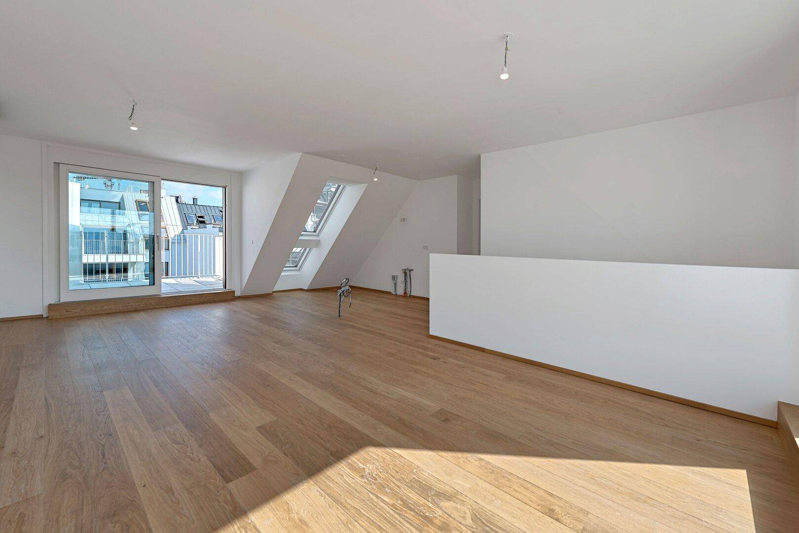 Offener Dachgeschossraum mit Holzboden, Dachfenstern und Zugang zur Außenterrasse.