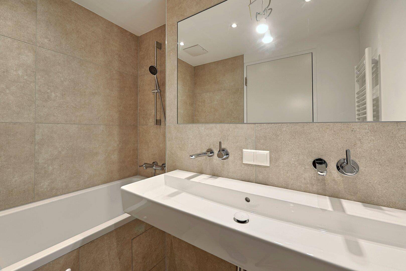 Modernes Badezimmer mit Badewanne, großem Waschtisch und beigefarbenen Fliesen.