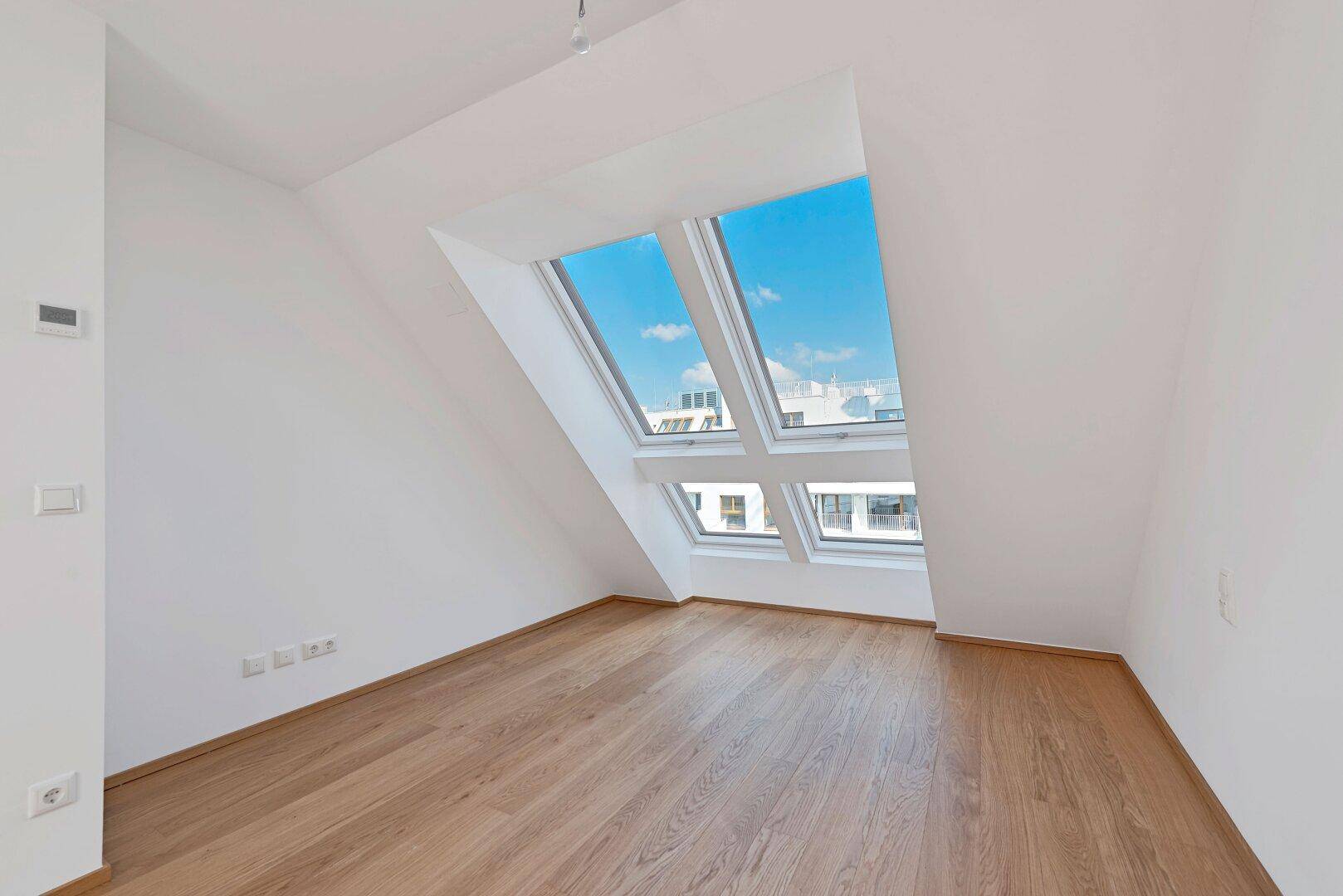 Helles Dachgeschosszimmer mit Holzboden und mehreren Dachfenstern für viel Tageslicht.