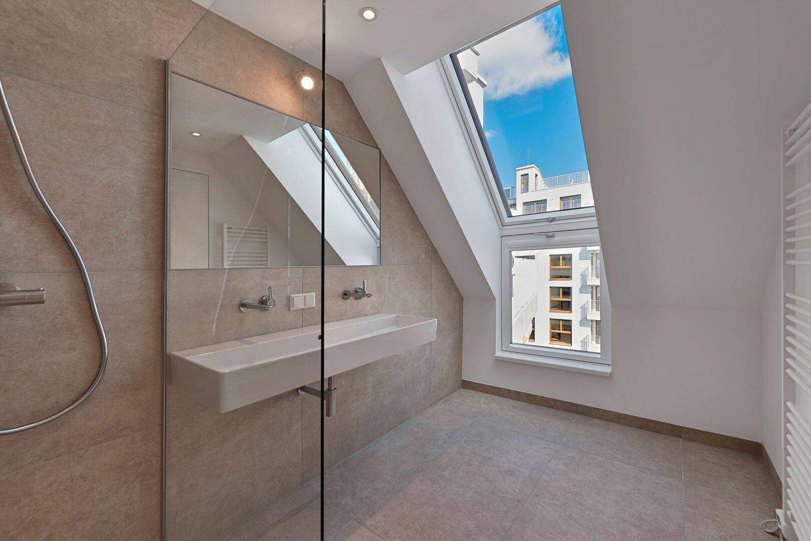 Modernes Badezimmer mit begehbarer Dusche, Waschtisch und Dachfenster für Helligkeit.