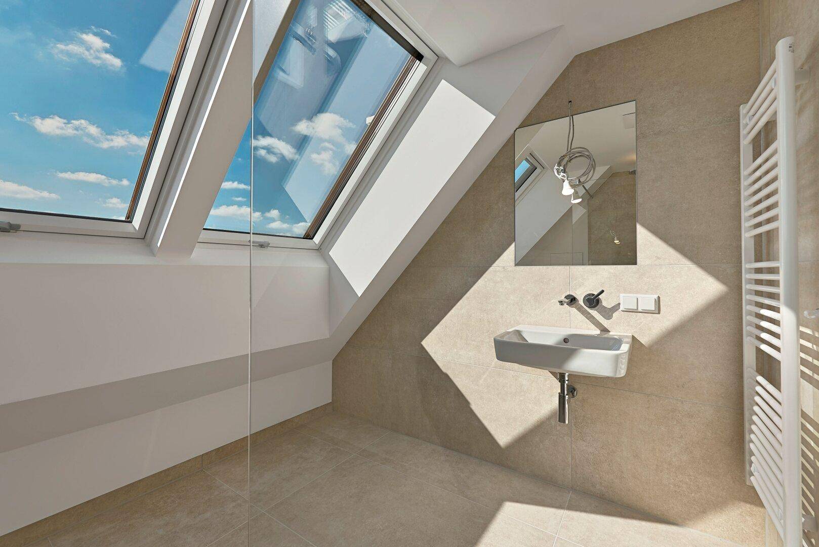 Helles Badezimmer mit kleinem Waschtisch, Dachfenster und beheiztem Handtuchhalter.