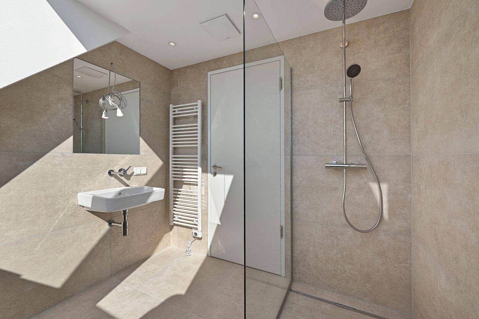 Modernes Badezimmer mit Regendusche, kleinem Waschtisch und beigefarbenen Fliesen.