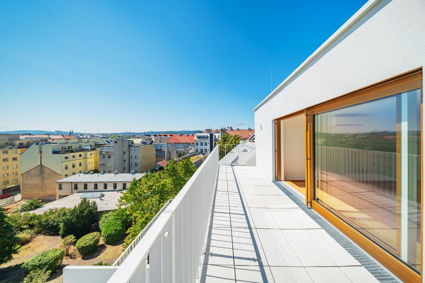 Lange Dachterrasse mit Fliesenboden und weitem Blick über die Stadtlandschaft.
