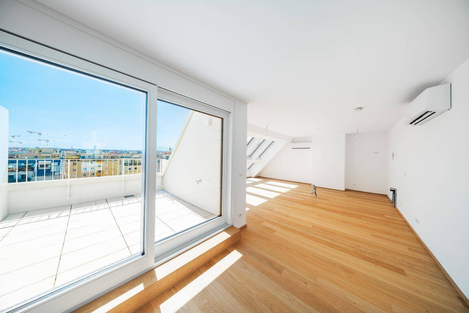 Geräumiger Wohnbereich mit Holzboden, Klimaanlage und großem Schiebefenster zur Terrasse mit Stadtblick.