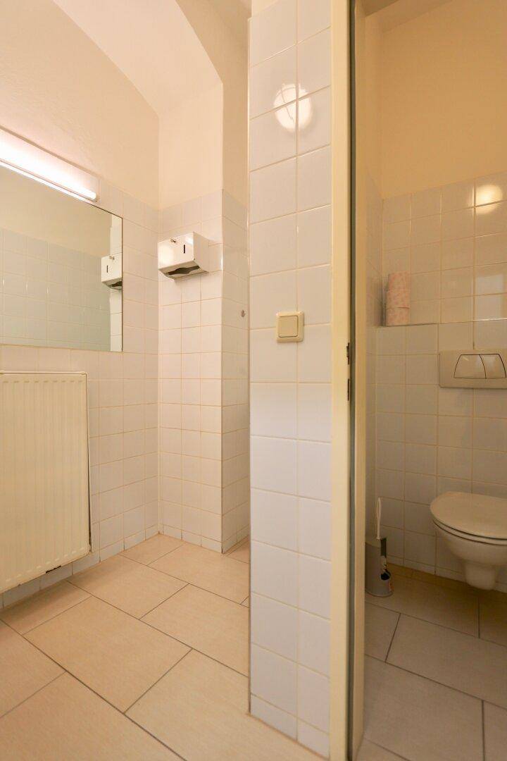 Gefliester Toilettenraum mit weißem WC, Heizkörper und einfacher Ausstattung.
