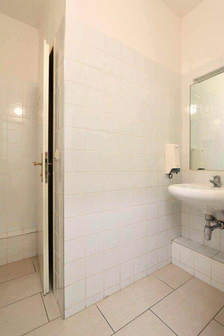 Heller Toilettenraum mit weißem Waschbecken, Spiegel und gefliesten Wänden.