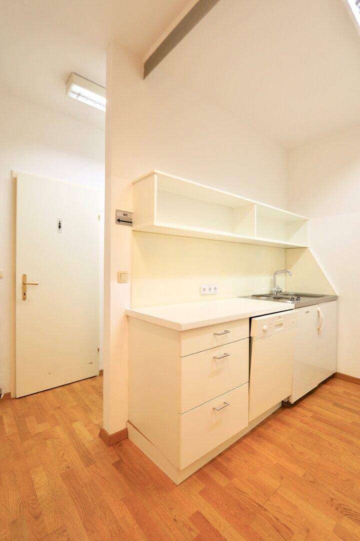 Kleine Küchenzeile mit weißen Schränken, Spüle und integriertem Geschirrspüler auf Parkettboden.