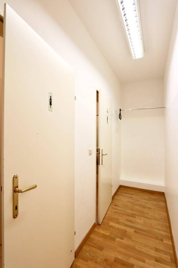 Heller Flur mit Parkettboden und Türen, eine davon führt zu den Damen-Toiletten.