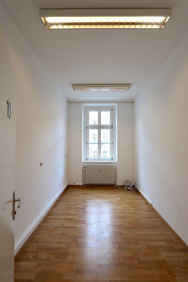 Schmaler, heller Raum mit Parkettboden und einem Fenster am Ende, geeignet als Einzelbüro.